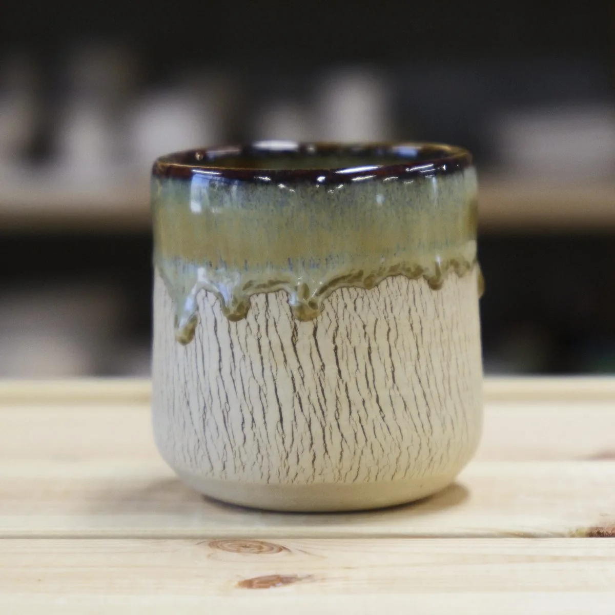 Handmade carved cup in cream clay with an olive glaze dripping from the rim.