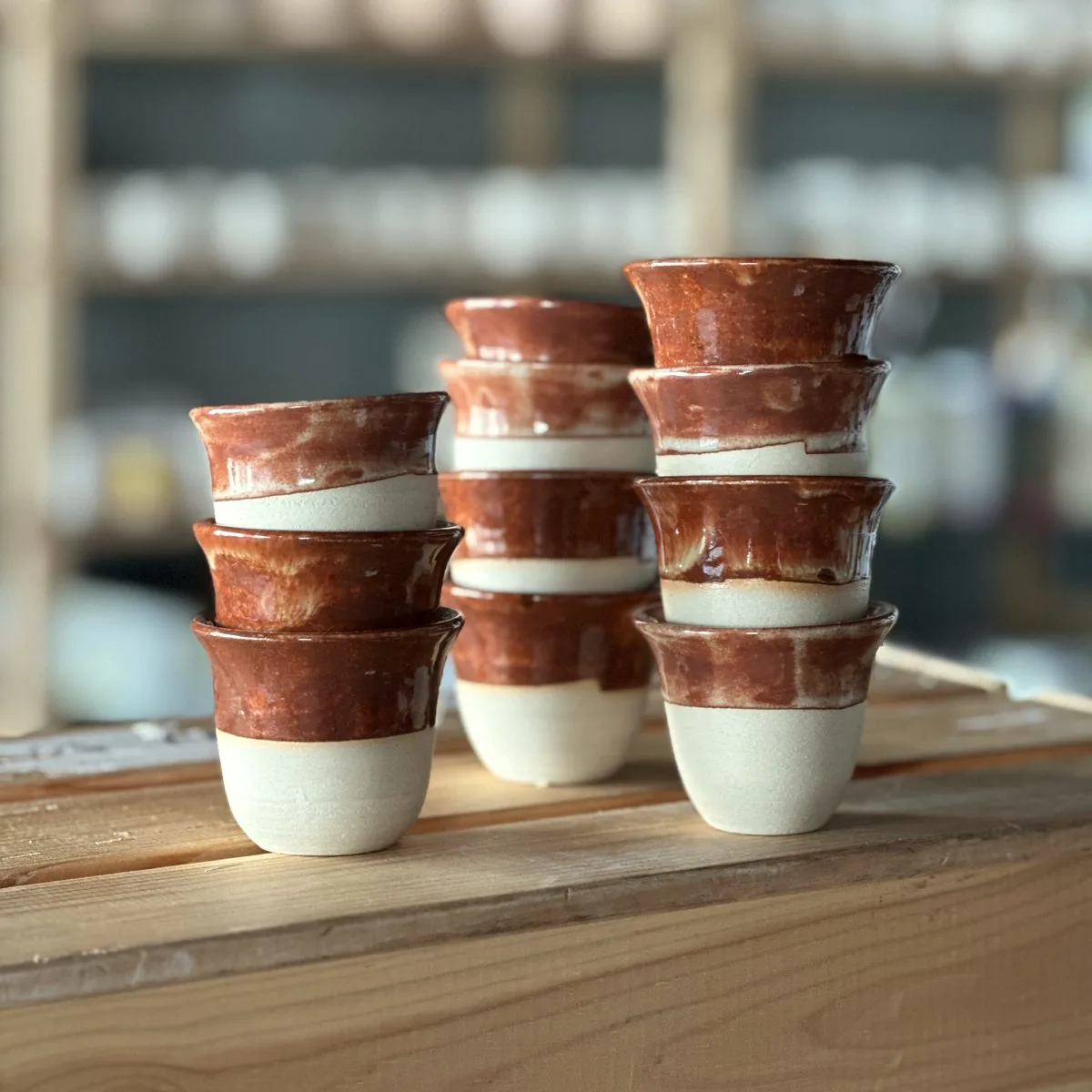 Stacks of small handmade finjan cups with a terracotta-red glaze and bare clay feet.