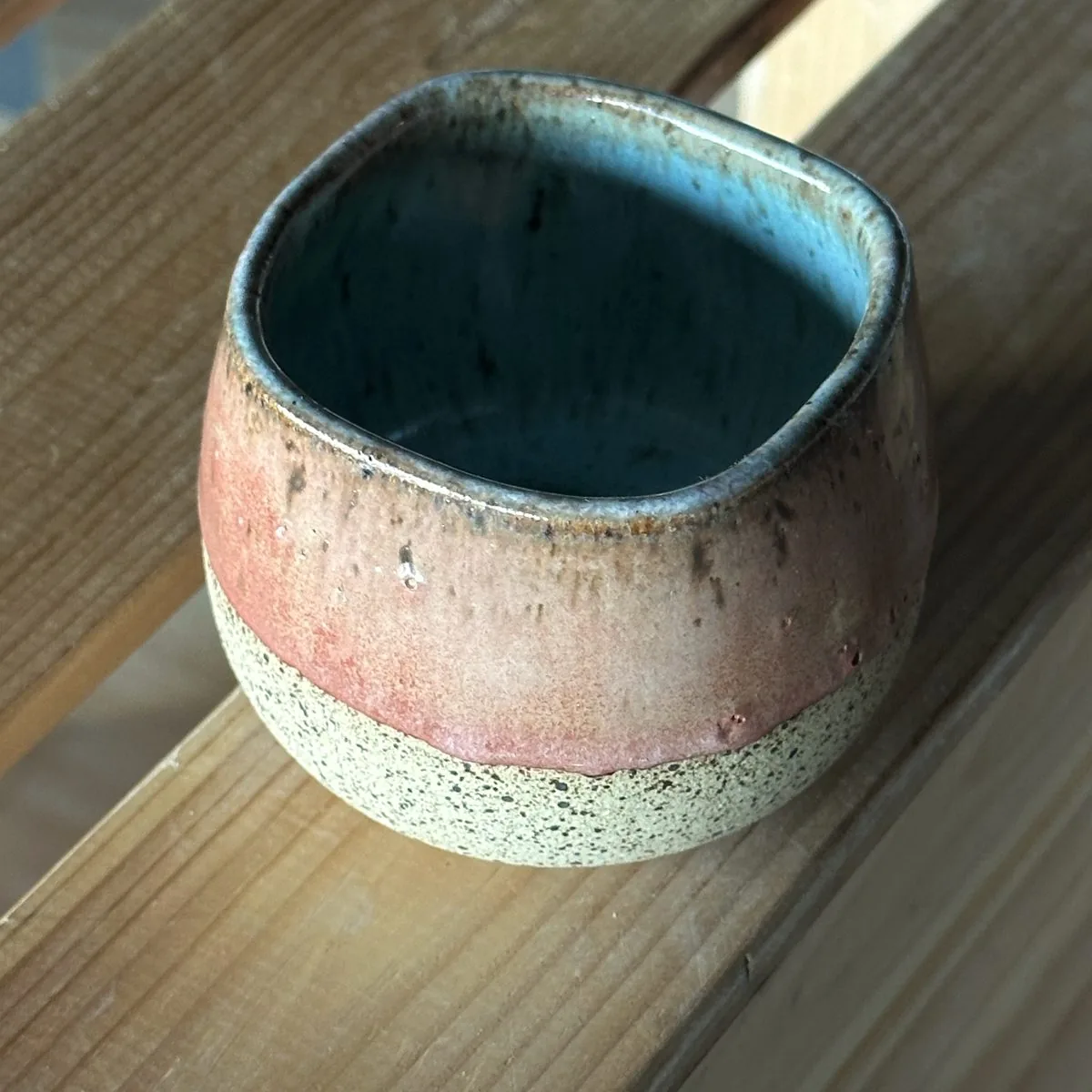 Handmade cup in a blush and terracotta glaze with a turquoise inside, in afternoon sun.
