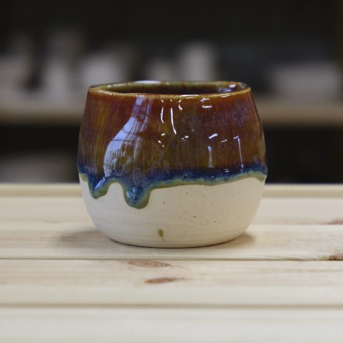 Small handmade cup with a glossy amber glaze and blue drips over a cream base.
