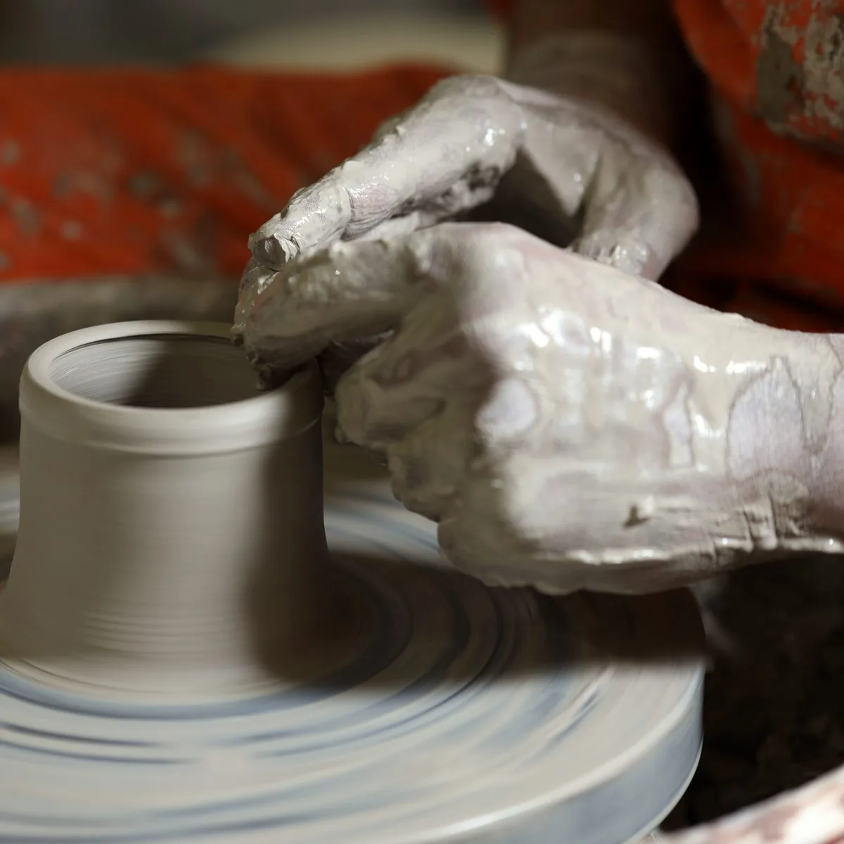 Making: clay-covered hands throwing a cup on the wheel.