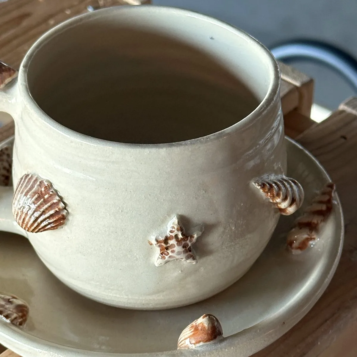The finished cup: a handmade cream cup and saucer decorated with clay seashells and a starfish.