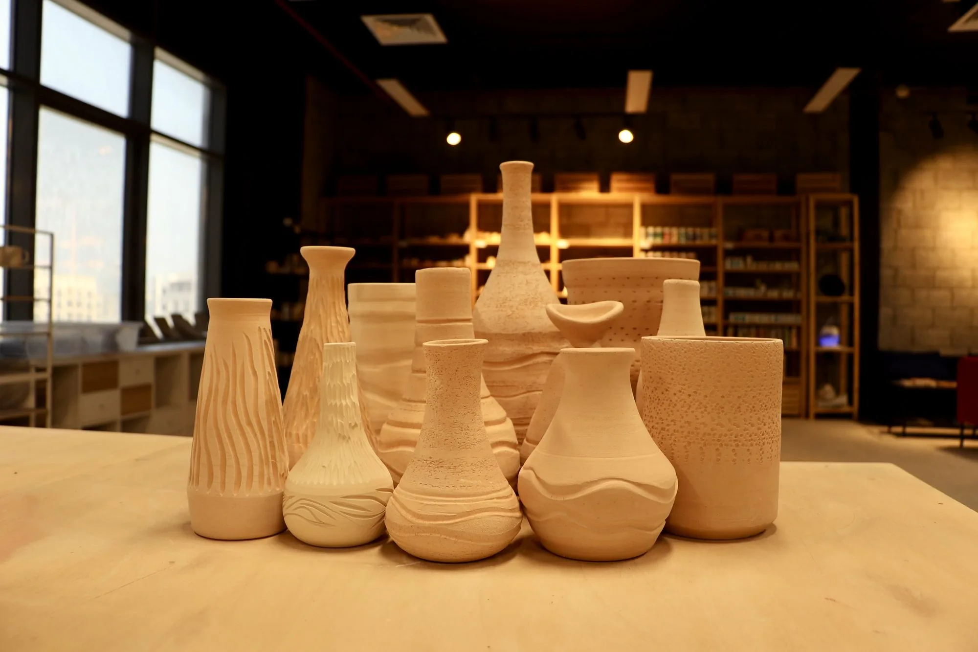 Unglazed handmade vases and cups gathered on a wooden table in the warm light of the studio.